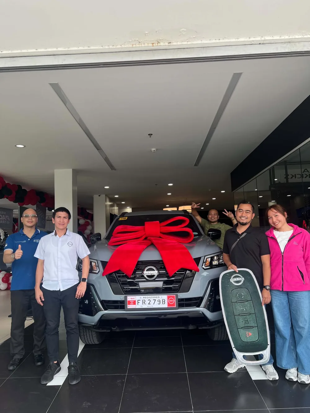 A group of new owners and staff posing with a ribboned Nissan on delivery day